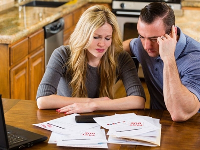 A couple worriedly looking at a stack of bills with “Past Due” stamps on them.
